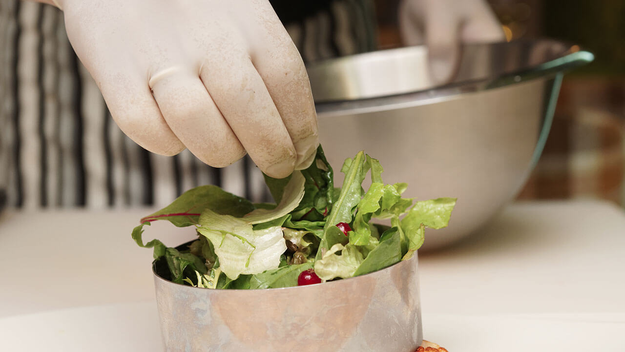 Closeup of gloved hand plating salad